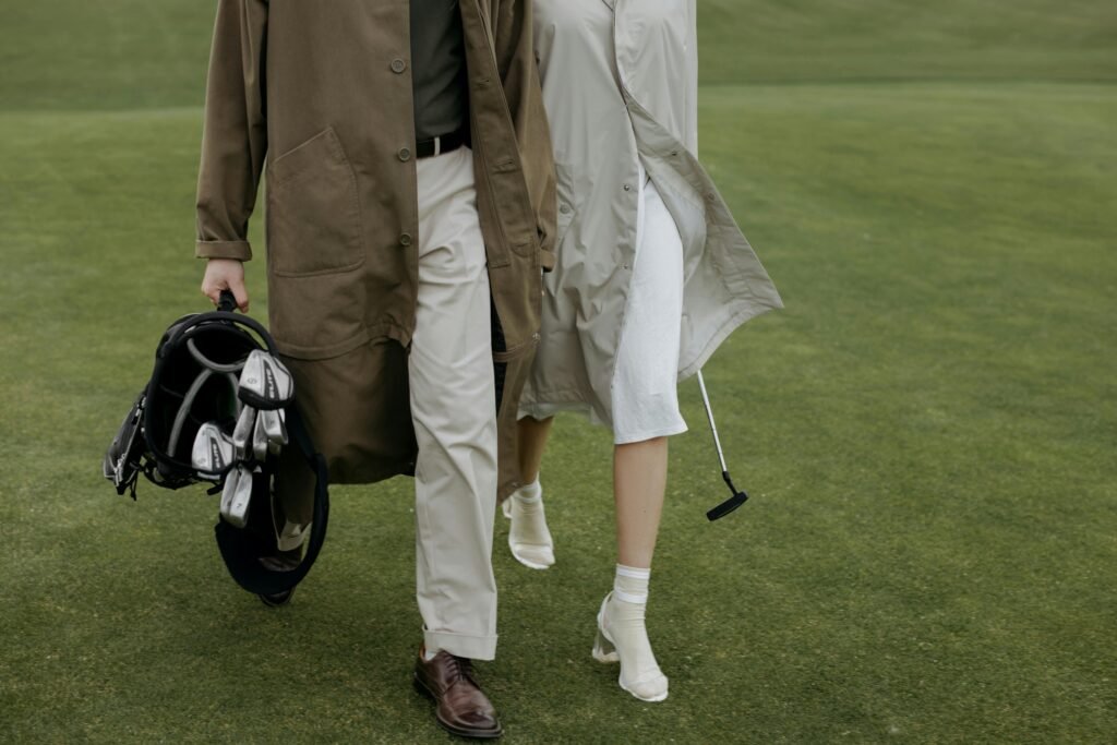 A stylish couple walking on a golf course, carrying a golf bag, highlighting fashion and leisure.