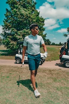 Welcome to Noble Fit Golf: My Must-Have Essentials for 2026 Male golfer in sunglasses walking across a sunny golf course with golf carts in Oklahoma City.